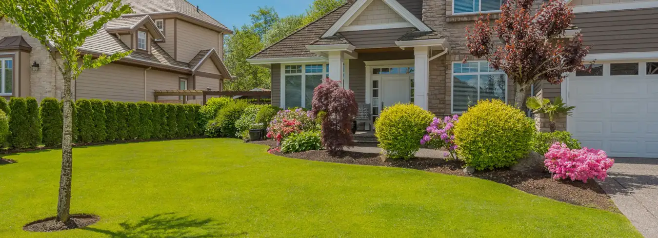 Large home with well-manicured green lawn and landscaped plants and shrubs. 